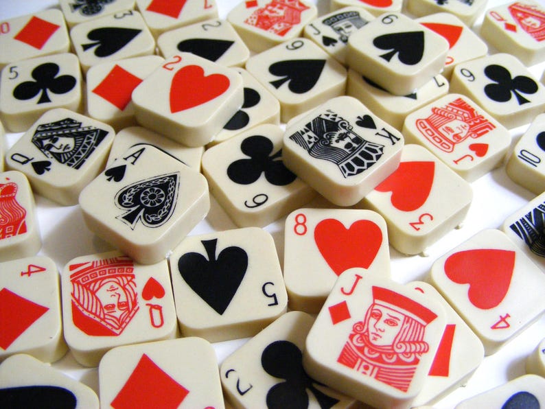 Pode incluir: Uma cole&ccedil;&atilde;o de pe&ccedil;as quadradas de cartas de jogar em branco sujo com s&iacute;mbolos de naipe vermelhos, pretos e brancos e figuras. As pe&ccedil;as est&atilde;o espalhadas, mostrando v&aacute;rios valores de cartas e naipes, incluindo espadas, cora&ccedil;&otilde;es, paus e ouros.