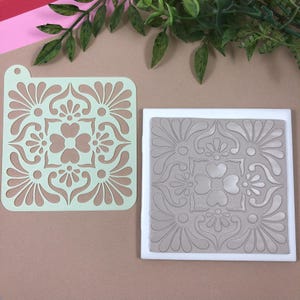 May include: A green plastic stencil with a decorative tile pattern and a gray clay tile with the same pattern embossed into it.