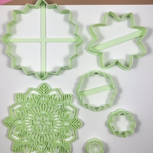 May include: Set of six green plastic cookie cutters in various shapes, including a circle, a star, a flower, and a mandala design.