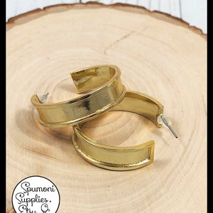 May include: A pair of gold hoop earrings with a thick, flat band. The earrings have a simple, modern design.