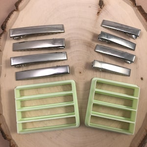 May include: A set of ten silver metal hair clips and two light green plastic molds for making hair clips. The molds have four rectangular slots.