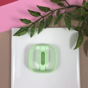 May include: A light green plastic cookie cutter shaped like the number zero. The cutter is on a white surface.