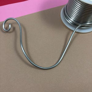 May include: A silver wire coil on a white spool, with a silver wire bent into a curved shape.