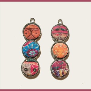 May include: Two silver pendant earrings with three round colorful patterned glass beads each. The beads are in shades of pink, orange, blue, and purple.