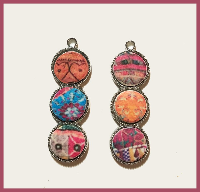 May include: Two silver pendant earrings with three round colorful patterned glass beads each. The beads are in shades of pink, orange, blue, and purple.