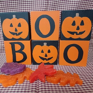May include: Wooden blocks spelling "BOO" with orange and black painted pumpkins. Each block has a different pumpkin design.