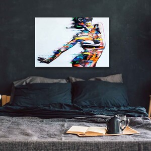 May include: Abstract painting of a person with colorful brushstrokes on a white background. The painting is framed and hanging on a dark wall above a bed.