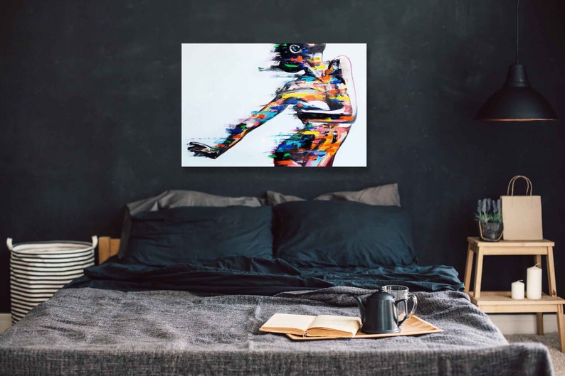 May include: Abstract painting of a person with colorful brushstrokes on a white background. The painting is framed and hanging on a dark wall above a bed.