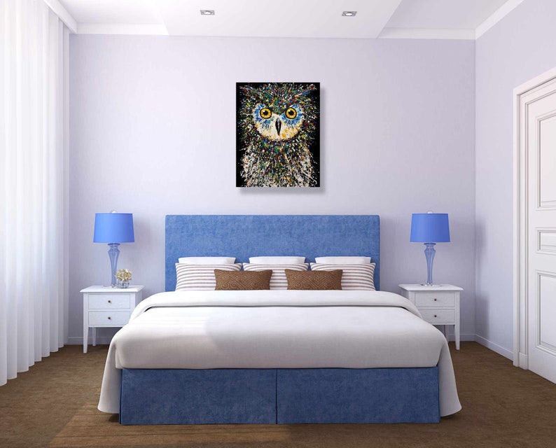 May include: A blue and white bedroom with a bed, two nightstands, and a painting of an owl above the bed. The owl is made of colorful dots and has yellow eyes.