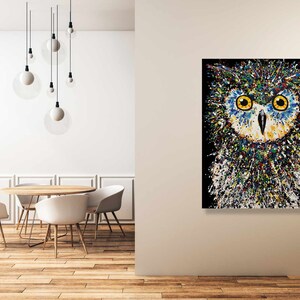 May include: A colorful abstract painting of an owl with yellow eyes. The owl is painted in a splatter style with a black background.