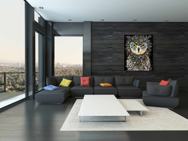 May include: A modern living room with a sectional sofa, a coffee table, and a side table. The wall behind the sofa is covered in dark wood paneling and features a colorful abstract painting of an owl. The room has large windows with a view of a city skyline.
