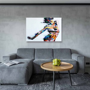 May include: A colorful abstract painting of a person with a white background. The painting is hanging on a gray wall above a gray couch and a coffee table with a bowl of green apples.