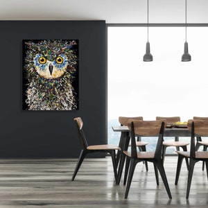May include: A colorful abstract painting of an owl with large, bright yellow eyes. The owl is painted in a splatter style with a black background.