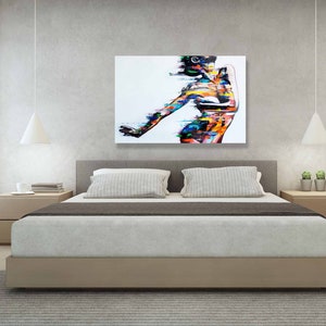 May include: Abstract painting of a person in a colorful, stylized pose. The painting is on a white canvas and is framed in a simple black frame. The painting is hanging on a wall in a bedroom setting.