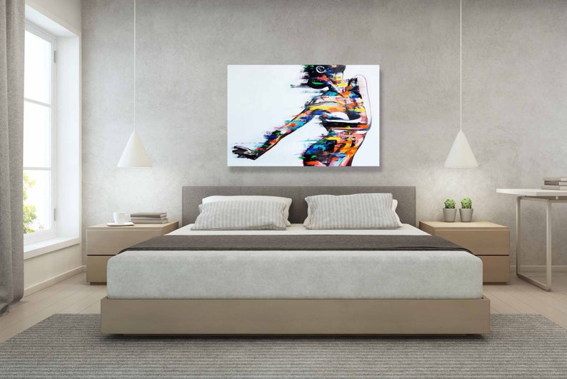 May include: Abstract painting of a person in a colorful, stylized pose. The painting is on a white canvas and is framed in a simple black frame. The painting is hanging on a wall in a bedroom setting.