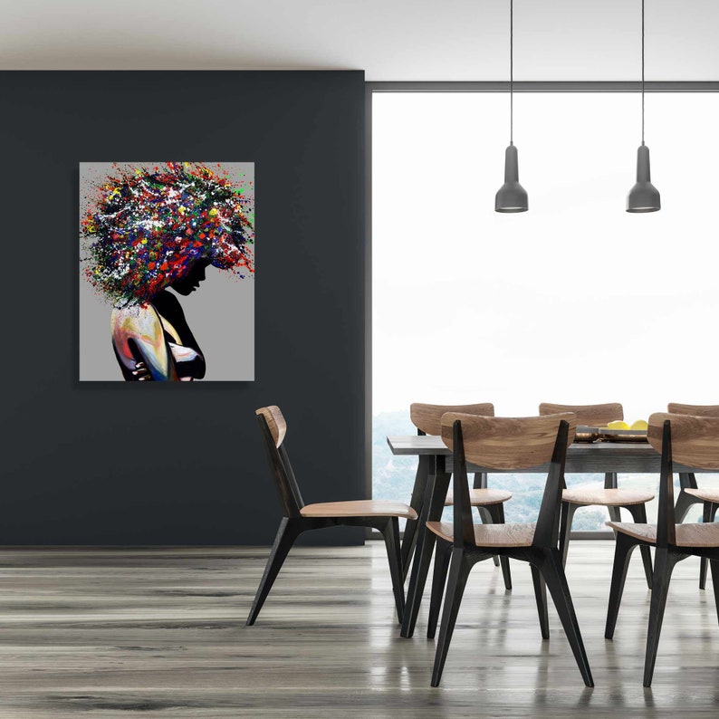 Puede incluir: Pintura abstracta de una mujer con el pelo de colores, colgada en una pared de un comedor con una mesa y sillas de madera.