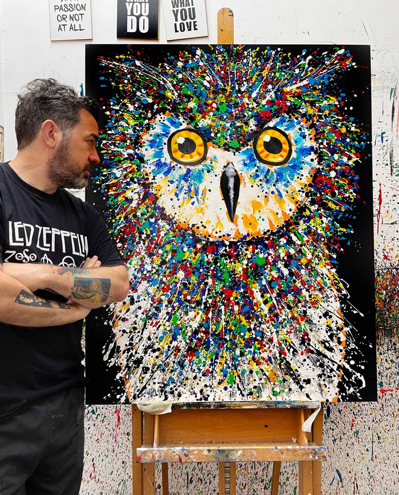 May include: A colorful abstract painting of an owl with a black background. The owl's eyes are yellow and the painting is done in a splatter paint style.