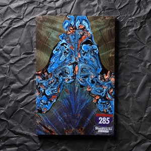 Op de afbeelding: Een rechthoekig blok donker hout met een centrale inleg van wervelende blauwe en koperkleurige hars. De houtnerf is zichtbaar aan de zijkanten. Een kleine sticker in de rechterbenedenhoek toont de tekst 285 Woodworks en SN 9514.