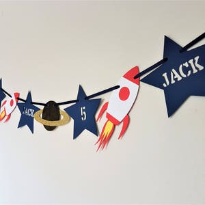 May include: A blue and gold space-themed banner with stars, planets, and rockets. The banner says "Jack" and "5" on it.