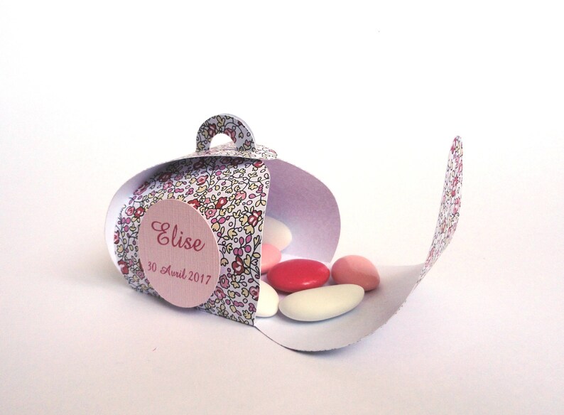 Pu&ograve; includere: Una scatola regalo bianca con un motivo floreale e un'etichetta rosa che dice "Elise 30 Avril 2017". La scatola &egrave; aperta e piena di confetti rosa e bianchi.