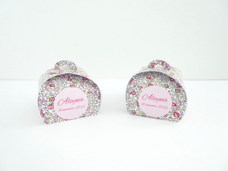Pu&ograve; includere: Due scatole regalo bianche con un motivo floreale e dettagli rosa. Ogni scatola ha un cerchio rosa con il nome "Aleyma" e la data "16 settembre 2022".