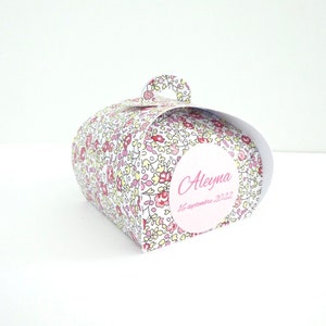 Pu&ograve; includere: Una scatola regalo bianca con un motivo floreale in tonalit&agrave; rosa, giallo e rosso. La scatola ha un manico e un'etichetta rotonda con il nome "Aleyna" e la data "16 settembre 2022" scritta in rosa.