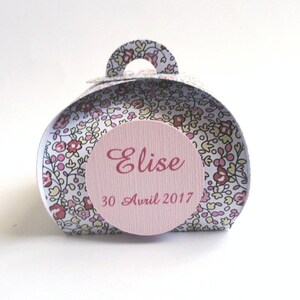 Pu&ograve; includere: Una piccola scatola regalo bianca con motivo floreale e un'etichetta circolare rosa che dice "Elise 30 Avril 2017".
