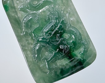 Op de afbeelding: Een jade hanger gegraveerd met een gedetailleerd drakenontwerp. De hanger is lichtgroen en heeft een gouden beugel.