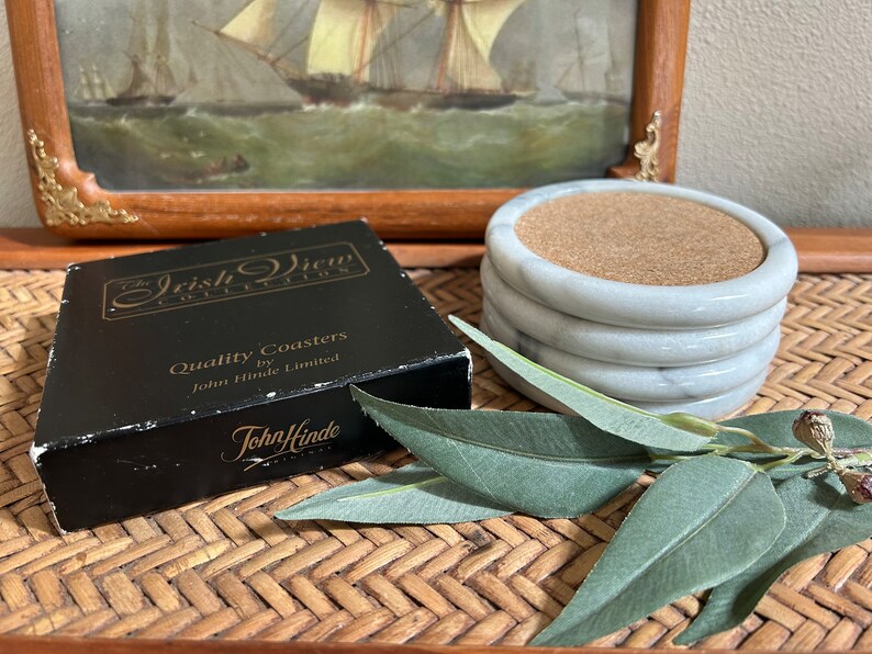 Pu&ograve; includere: Un set di quattro sottobicchieri in marmo bianco con inserti in sughero. I sottobicchieri sono confezionati in una scatola nera con il testo "The Irish View Collection" e "Quality Coasters by John Hinde Limited".