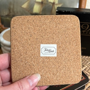 Pu&ograve; includere: Un sottobicchiere in sughero marrone con un'etichetta bianca che dice "John Hinde Originals".