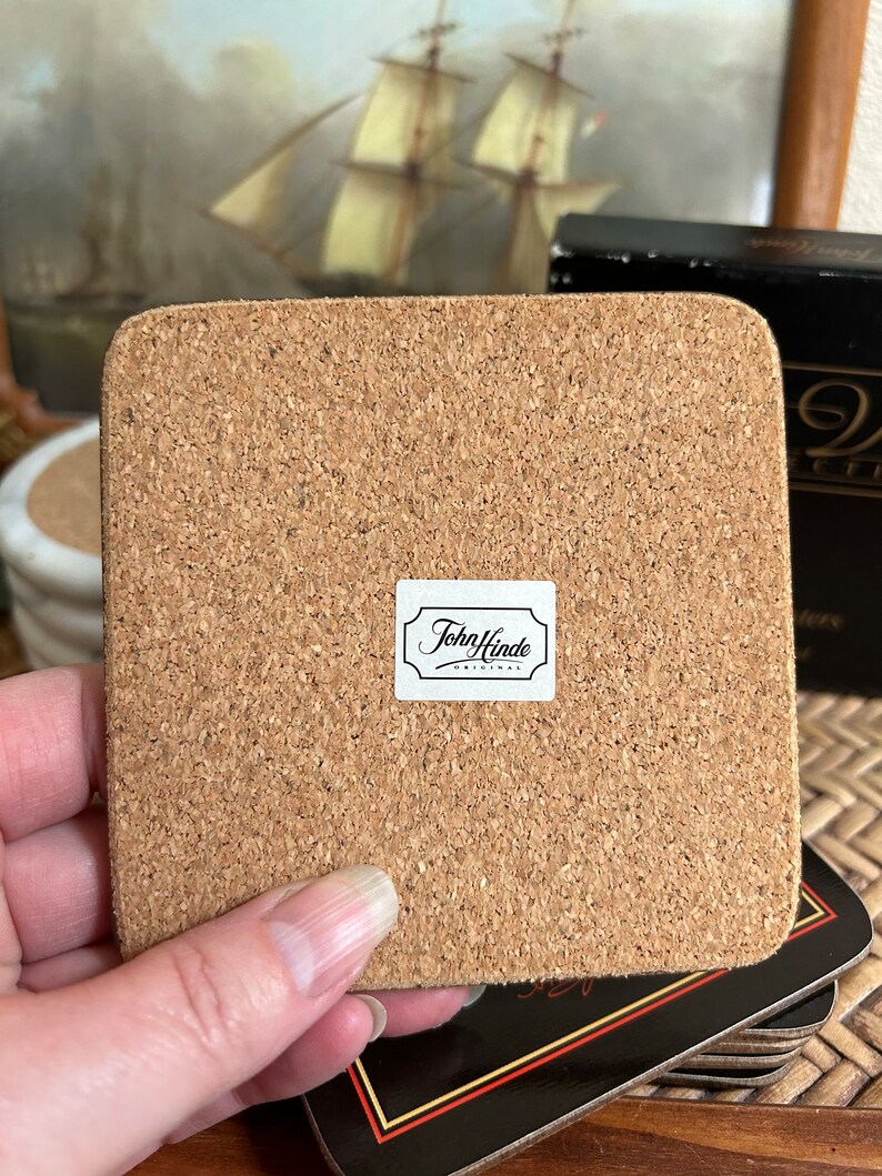 Pu&ograve; includere: Un sottobicchiere in sughero marrone con un'etichetta bianca che dice "John Hinde Originals".