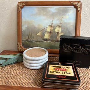 Pu&ograve; includere: Set di quattro sottobicchieri in marmo bianco con inserti in sughero. I sottobicchieri sono confezionati in una scatola nera con lettere dorate che recitano "The Irish View Collection" e "Quality Coasters by Limited". &Egrave; anche raffigurato un sottobicchiere separato con sfondo nero e lettere dorate che recitano "Guinness & Co. In Bottle Extra Stout".