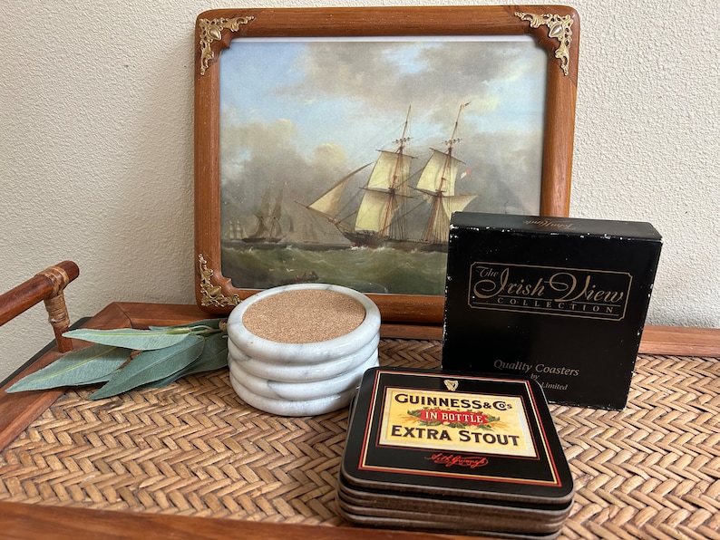 Pu&ograve; includere: Set di quattro sottobicchieri in marmo bianco con inserti in sughero. I sottobicchieri sono confezionati in una scatola nera con lettere dorate che recitano "The Irish View Collection" e "Quality Coasters by Limited". &Egrave; anche raffigurato un sottobicchiere separato con sfondo nero e lettere dorate che recitano "Guinness & Co. In Bottle Extra Stout".