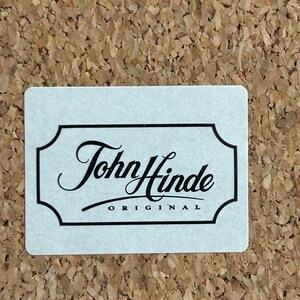 Pu&ograve; includere: Un'etichetta bianca con un bordo nero e il testo "John Hinde ORIGINAL" in un carattere corsivo.