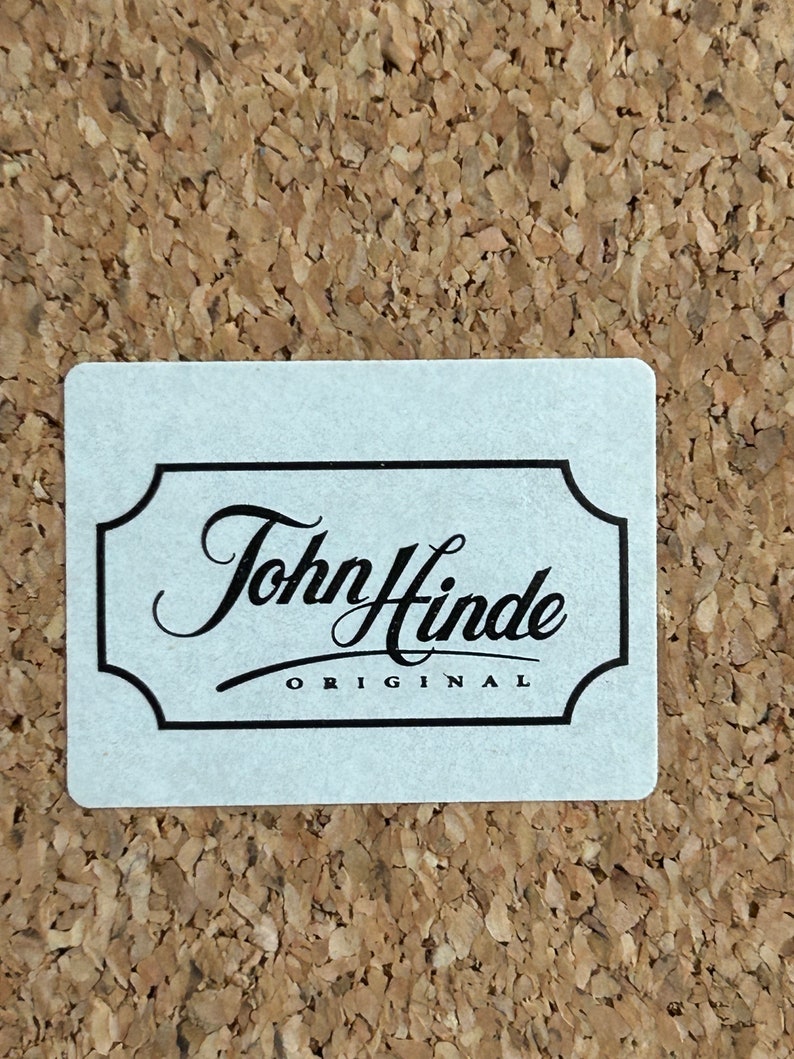 Pu&ograve; includere: Un'etichetta bianca con un bordo nero e il testo "John Hinde ORIGINAL" in un carattere corsivo.