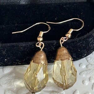 May include: A pair of gold tone dangle earrings with teardrop shaped clear glass beads. The beads have a faceted design and a light amber color.