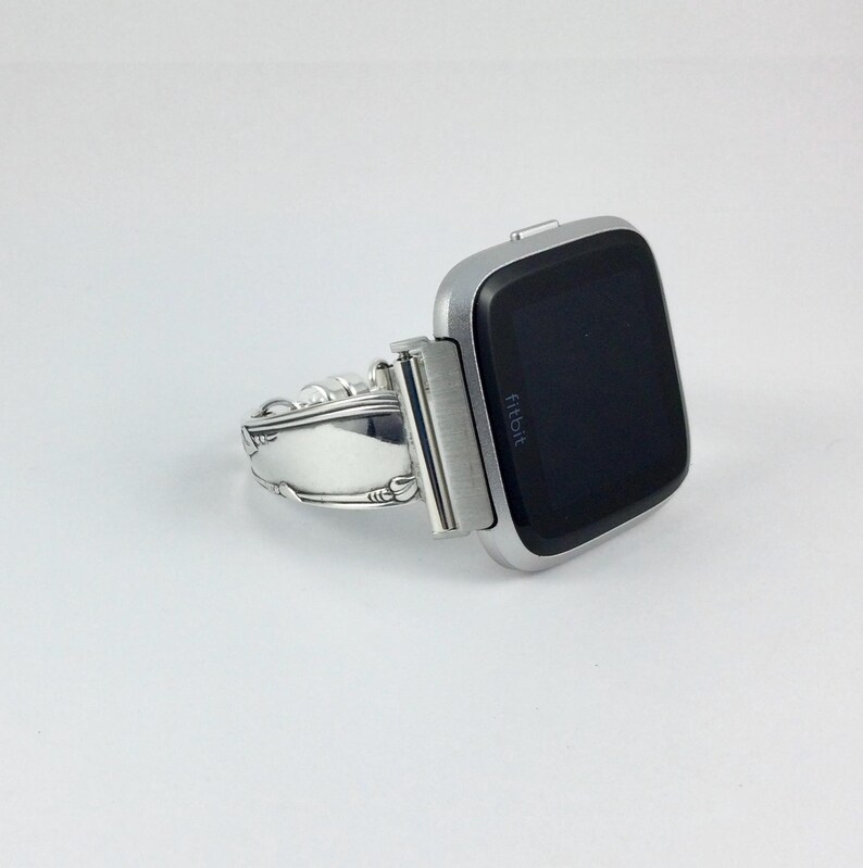 Peut inclure: Une montre connect&eacute;e Fitbit argent&eacute;e avec un bracelet personnalis&eacute; fabriqu&eacute; &agrave; partir d'une pi&egrave;ce d'argenterie reconditionn&eacute;e.