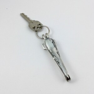 May include: Silver key chain with a key and a spoon handle. The spoon handle has a decorative design.