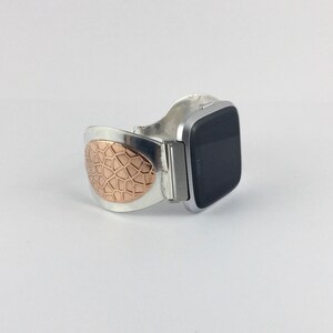 May include: A silver and rose gold watch band with a geometric pattern. The band is designed to fit a square-shaped smartwatch.