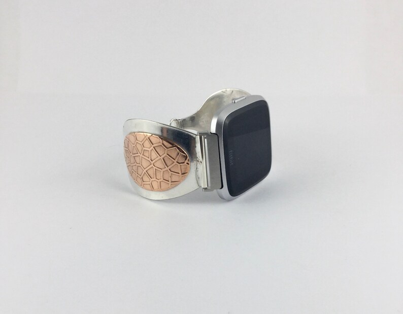 May include: A silver and rose gold watch band with a geometric pattern. The band is designed to fit a square-shaped smartwatch.