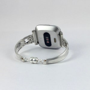 May include: Silver watch band with a floral design. The band is made of a spoon and has a magnetic clasp.