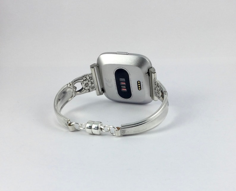 May include: Silver watch band with a floral design. The band is made of a spoon and has a magnetic clasp.
