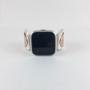 May include: A silver smartwatch with a black screen and a silver band with copper accents. The band has a unique design with a textured pattern.
