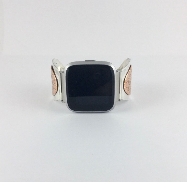 May include: A silver smartwatch with a black screen and a silver band with copper accents. The band has a unique design with a textured pattern.