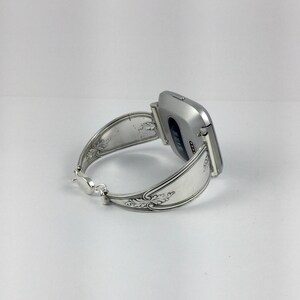 May include: A silver smartwatch with a silver spoon band. The band is decorated with an ornate design.