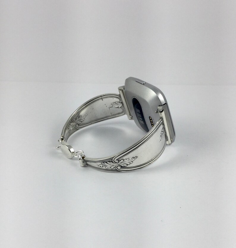 May include: A silver smartwatch with a silver spoon band. The band is decorated with an ornate design.