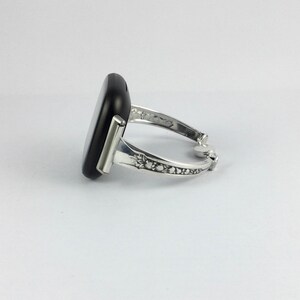Puede incluir: Un brazalete de plata con una piedra rectangular negra engastada en la parte delantera. El brazalete tiene un dise&ntilde;o decorativo en la banda.