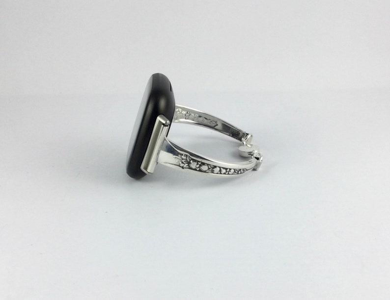 Puede incluir: Un brazalete de plata con una piedra rectangular negra engastada en la parte delantera. El brazalete tiene un dise&ntilde;o decorativo en la banda.