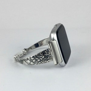 May include: A silver watch band with a floral design. The band is made of metal and has a polished finish.