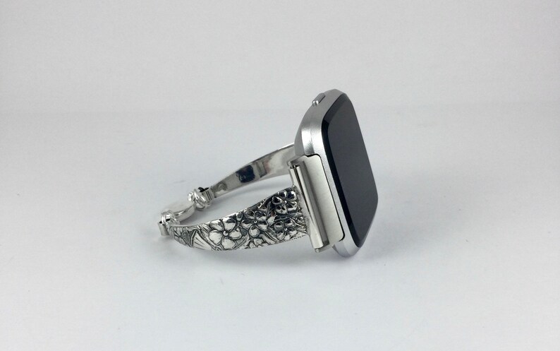 May include: A silver watch band with a floral design. The band is made of metal and has a polished finish.
